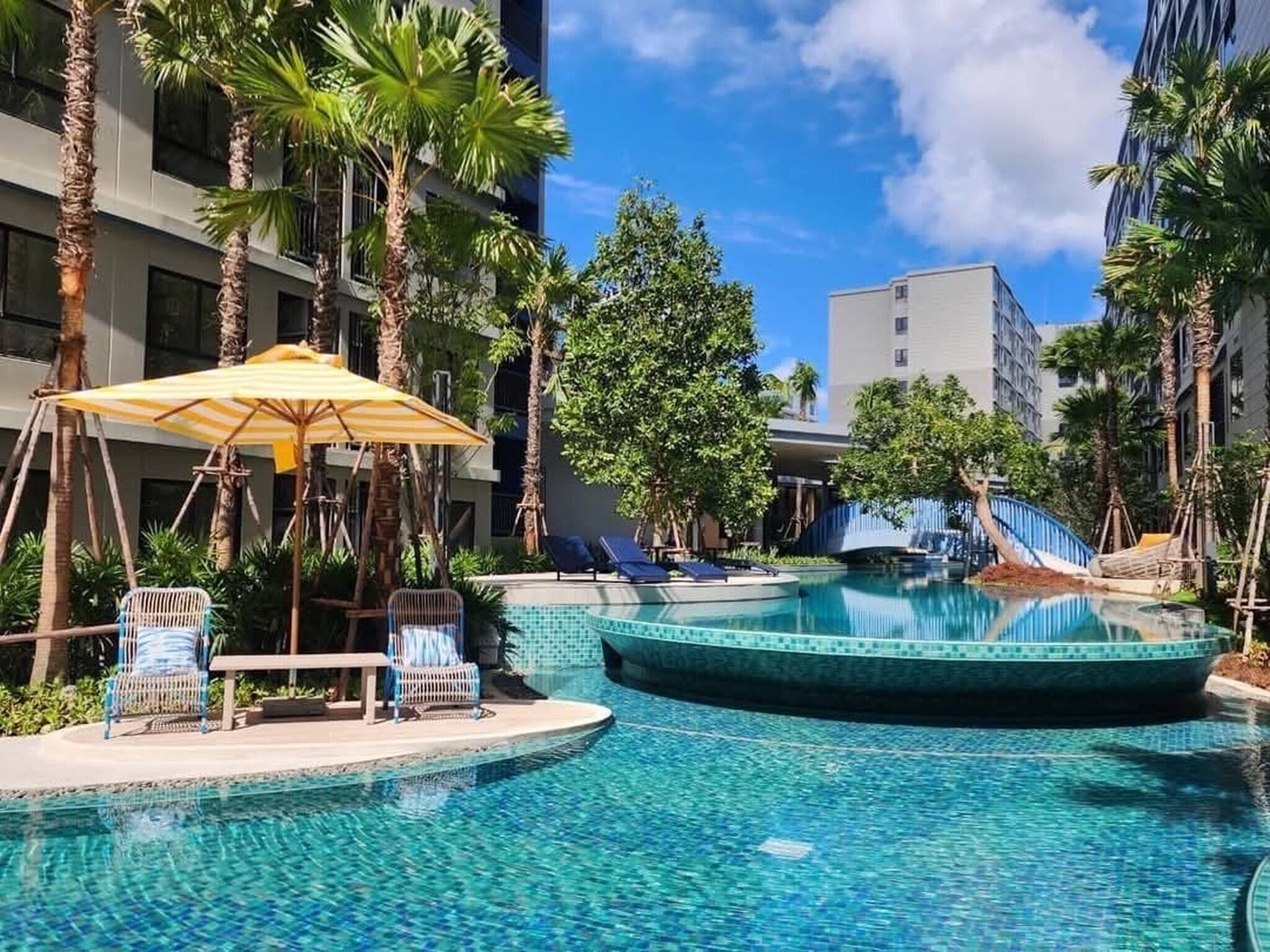 A pool area with lounge chairs, a sun umbrella, and palm trees.