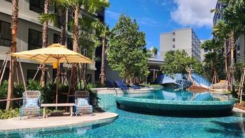 A pool area with lounge chairs, a sun umbrella, and palm trees.