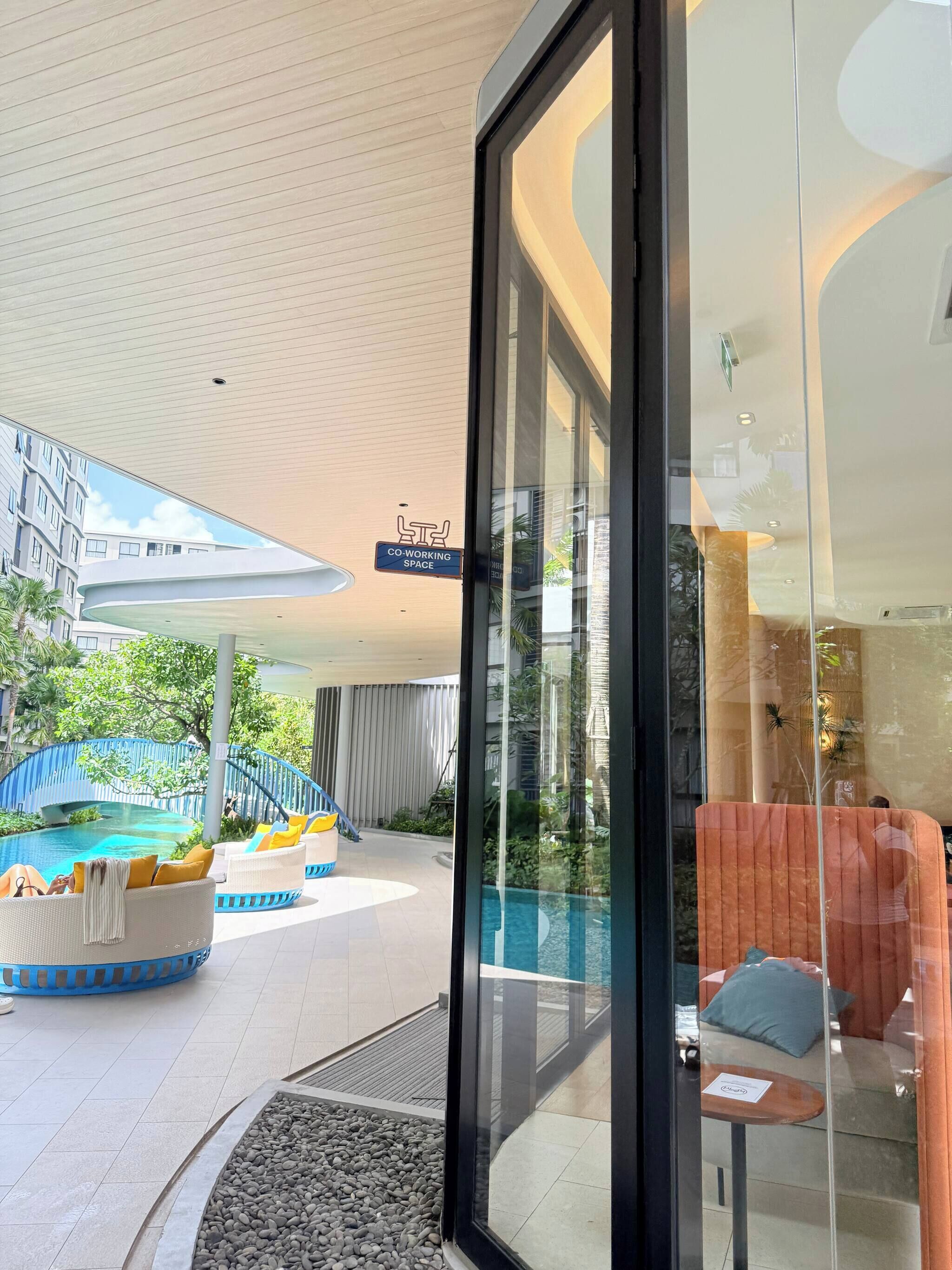 A modern hotel with a glass entrance, a pool area with lounge chairs, and a sign indicating a co-working space.