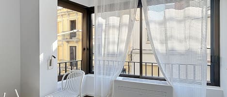 A balcony with a white chair, a small table, and a window with white curtains.