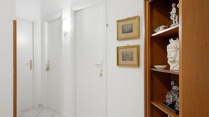 Ein Korridor mit weißen Türen, einem Holzschrank mit Skulpturen und zwei gerahmten Bildern an der Wand.