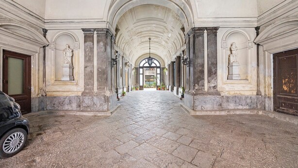 Ein Korridor mit Steinboden, gewölbter Decke und Statuen an jeder Seite.