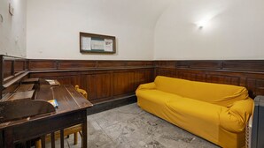 Ein Zimmer mit einer hölzernen Bank, einem gelben Sofa, einer Holzkommode und einem Korkbrett an der Wand.