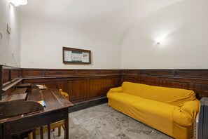 A room with a wooden bench, a yellow sofa, a wooden cabinet, and a bulletin board on the wall. - Apartment 'Al Palazzo Del Principe Al Massimo' with Wi-Fi and Air Conditioning (Palermo)