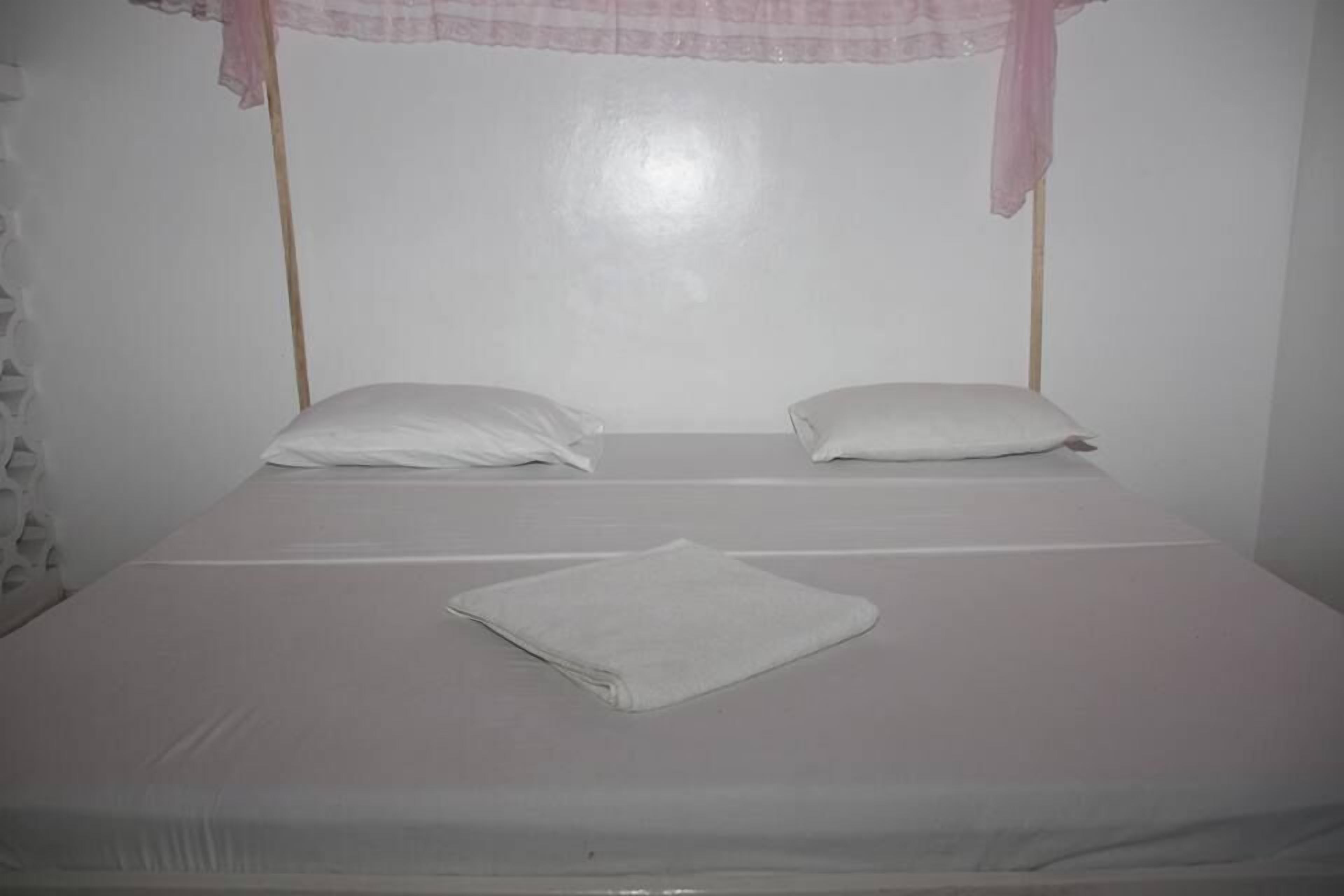 Un lit simple avec un matelas blanc, deux oreillers et une serviette blanche pliée.
