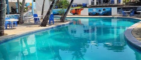 Una piscina con agua cristalina azul, rodeada de palmeras y sillas azules.