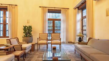 A room with a sofa, chairs, a table, a potted plant, and a window with curtains.