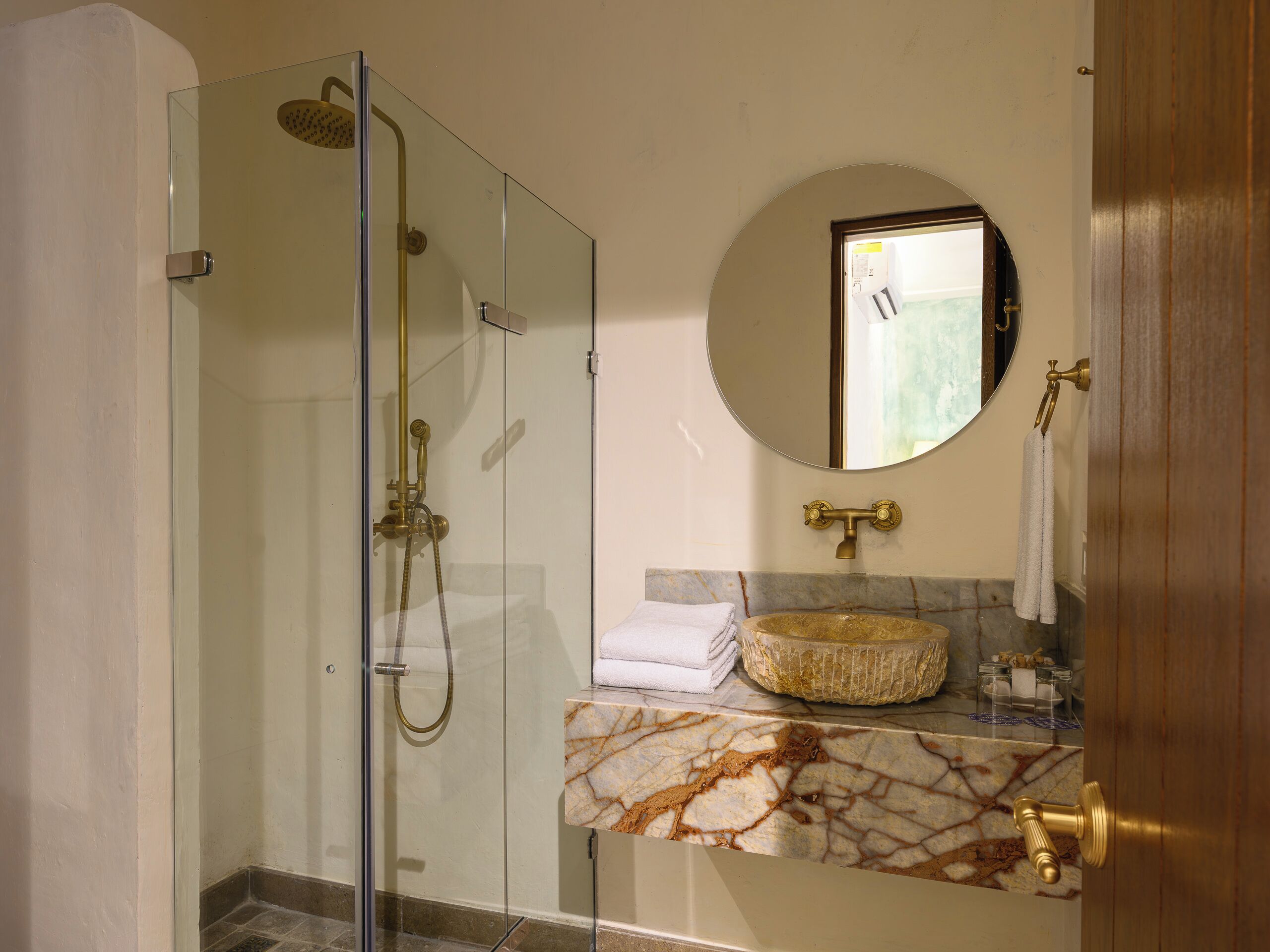 A bathroom with a glass-enclosed shower, a marble sink, and a round mirror.