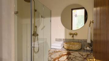A bathroom with a glass-enclosed shower, a marble sink, and a round mirror.