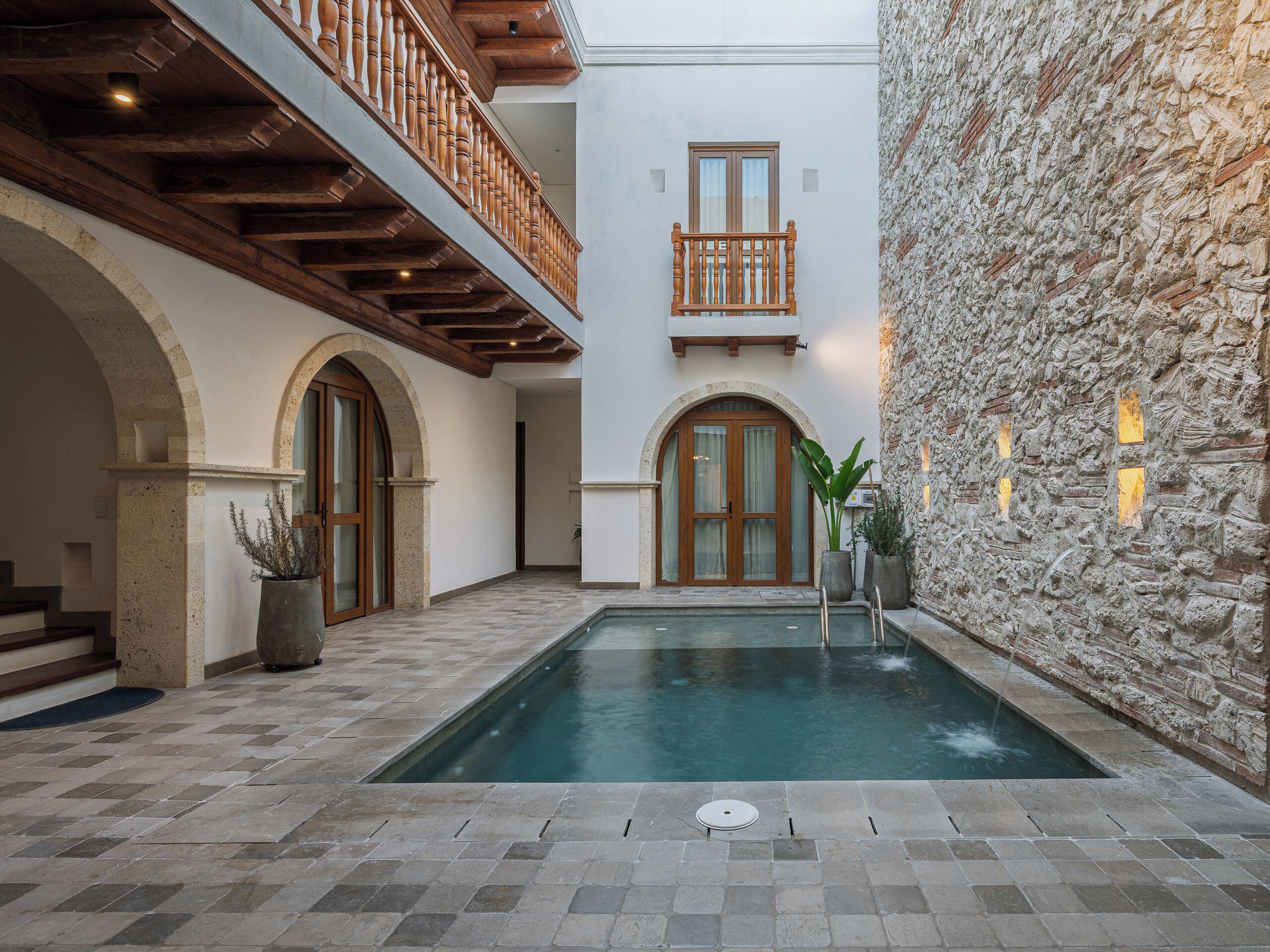 Una zona de piscina con paredes de piedra, balcones de madera y puertas arqueadas.