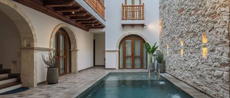 Una zona de piscina con paredes de piedra, balcones de madera y puertas arqueadas.