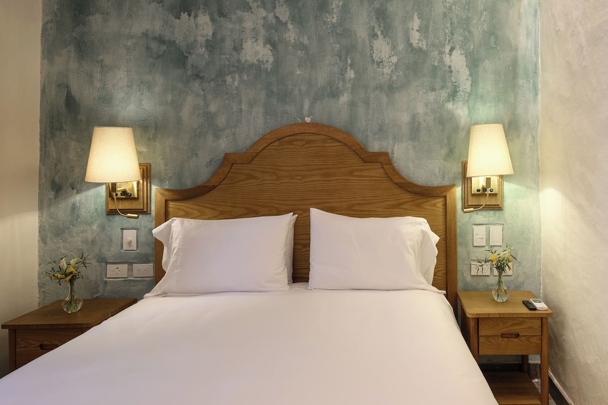 Una cama con dos almohadas blancas, un cabecero de madera y dos mesitas de noche con lámparas y jarrones.