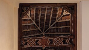 Een houten deur met ingewikkelde geometrische patronen en een kroonluchter met meerdere lichtpunten.