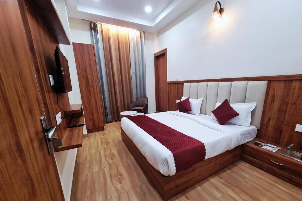 A hotel room with a wooden bed, a TV, a chair, and a window with curtains.
