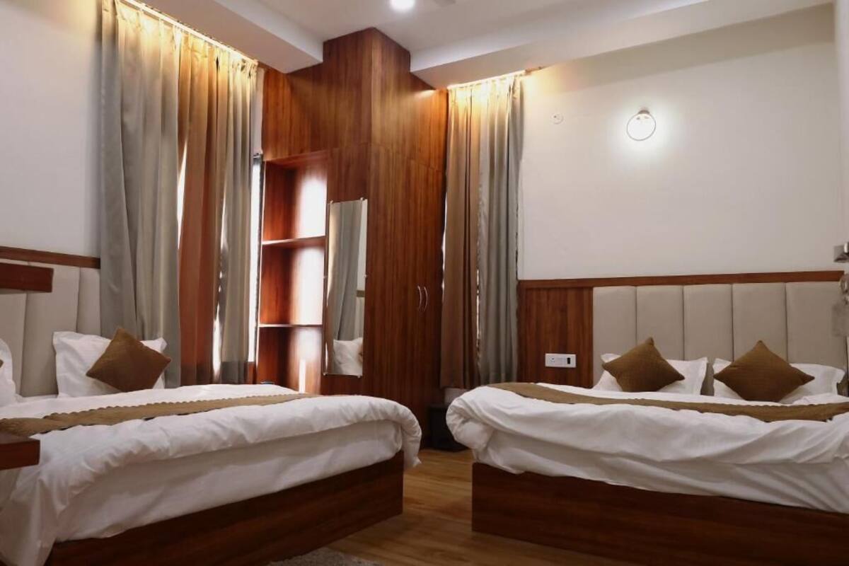 A hotel room with two beds, wooden headboards, a wardrobe, and a mirror.