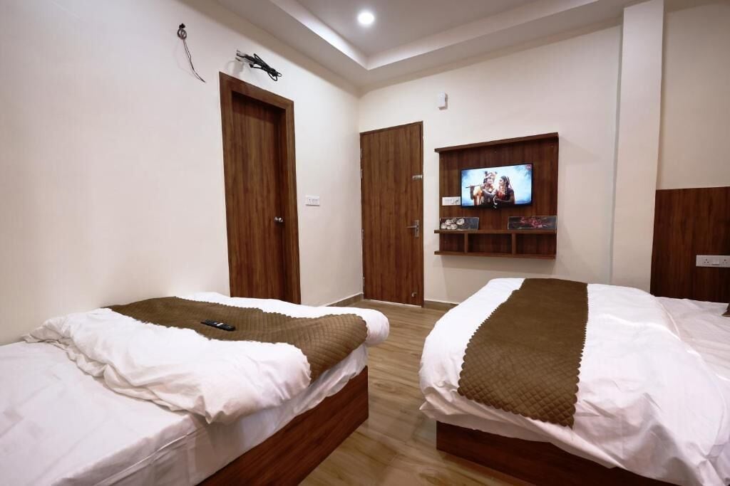 A hotel room with two beds, a TV mounted on the wall, wooden doors, and a ceiling light.