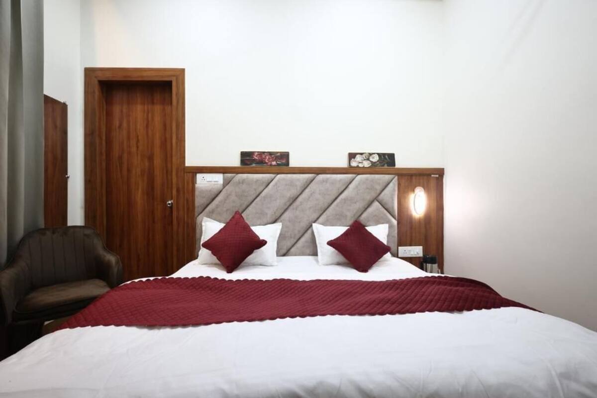 A hotel room with a bed, a wooden headboard, a red blanket, a brown leather chair, and a wooden door.