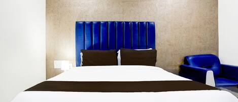 A hotel room with a large bed, a blue headboard, a blue armchair, and a wall-mounted air conditioning unit.