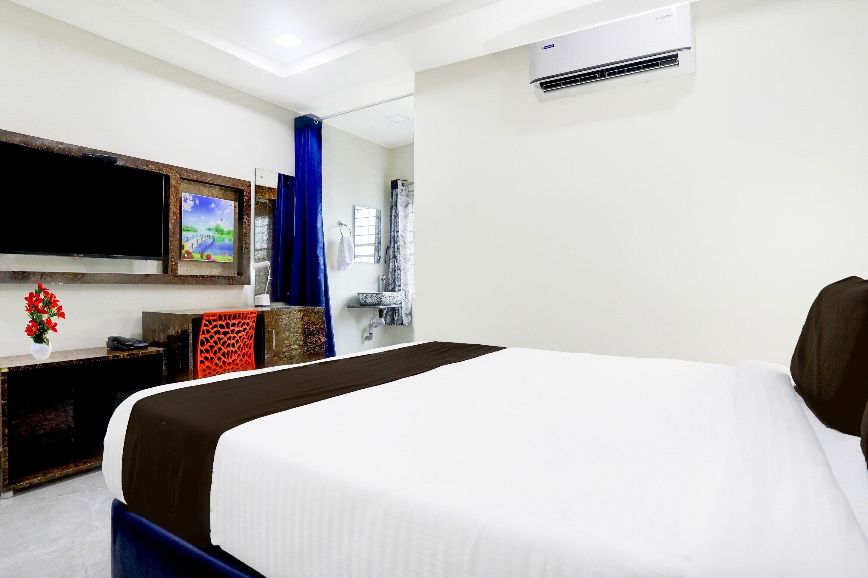 A hotel room with a bed, a TV, a painting, and an air conditioning unit.
