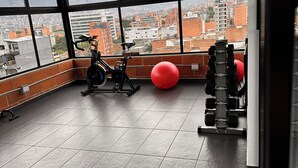Ein Fitnessstudio mit Trainingsgeräten, einem roten Balanceball und Blick auf eine Stadtlandschaft durch große Fenster.