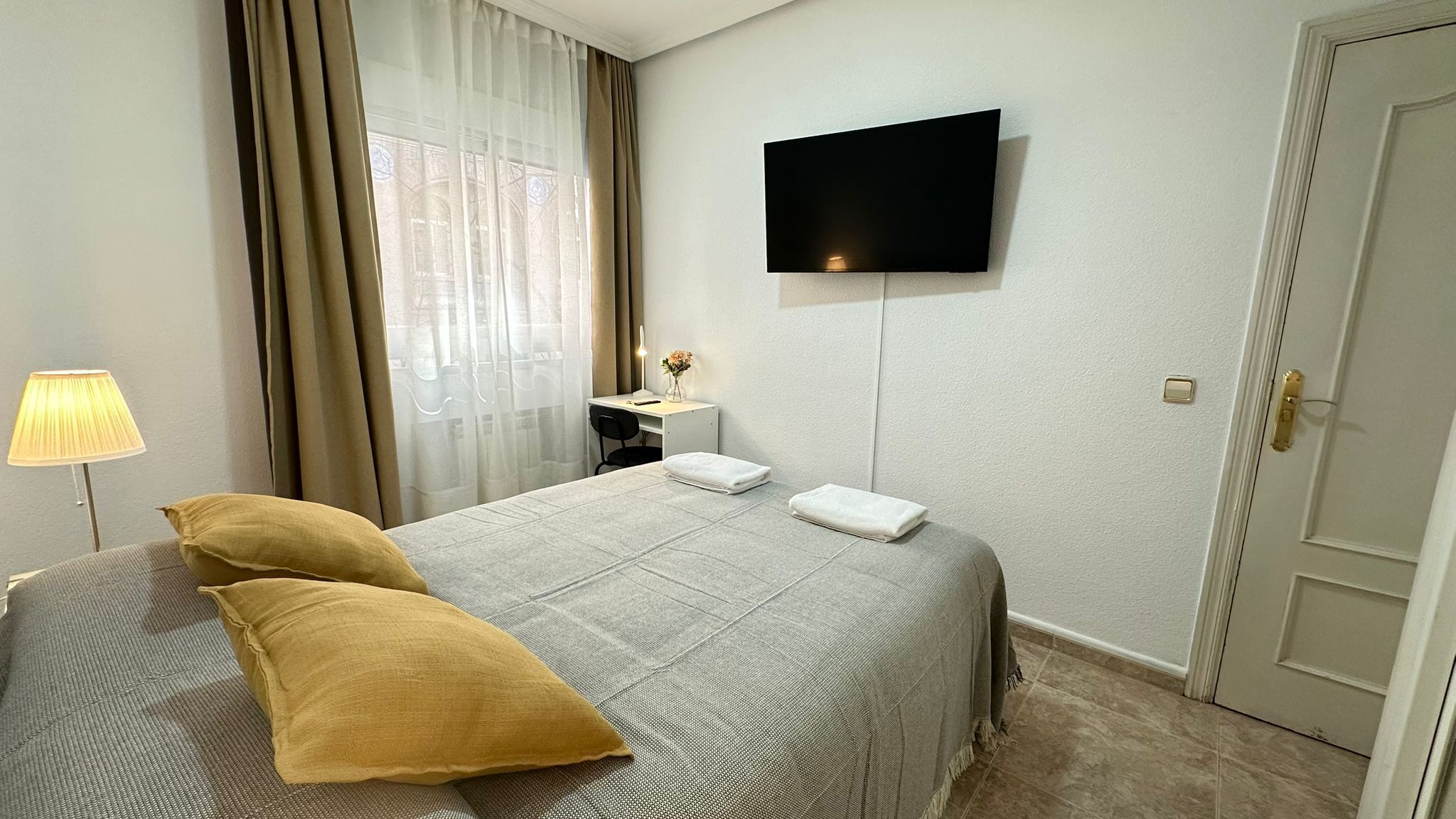 Una habitación de hotel con cama, escritorio con lámpara, televisión y puerta.