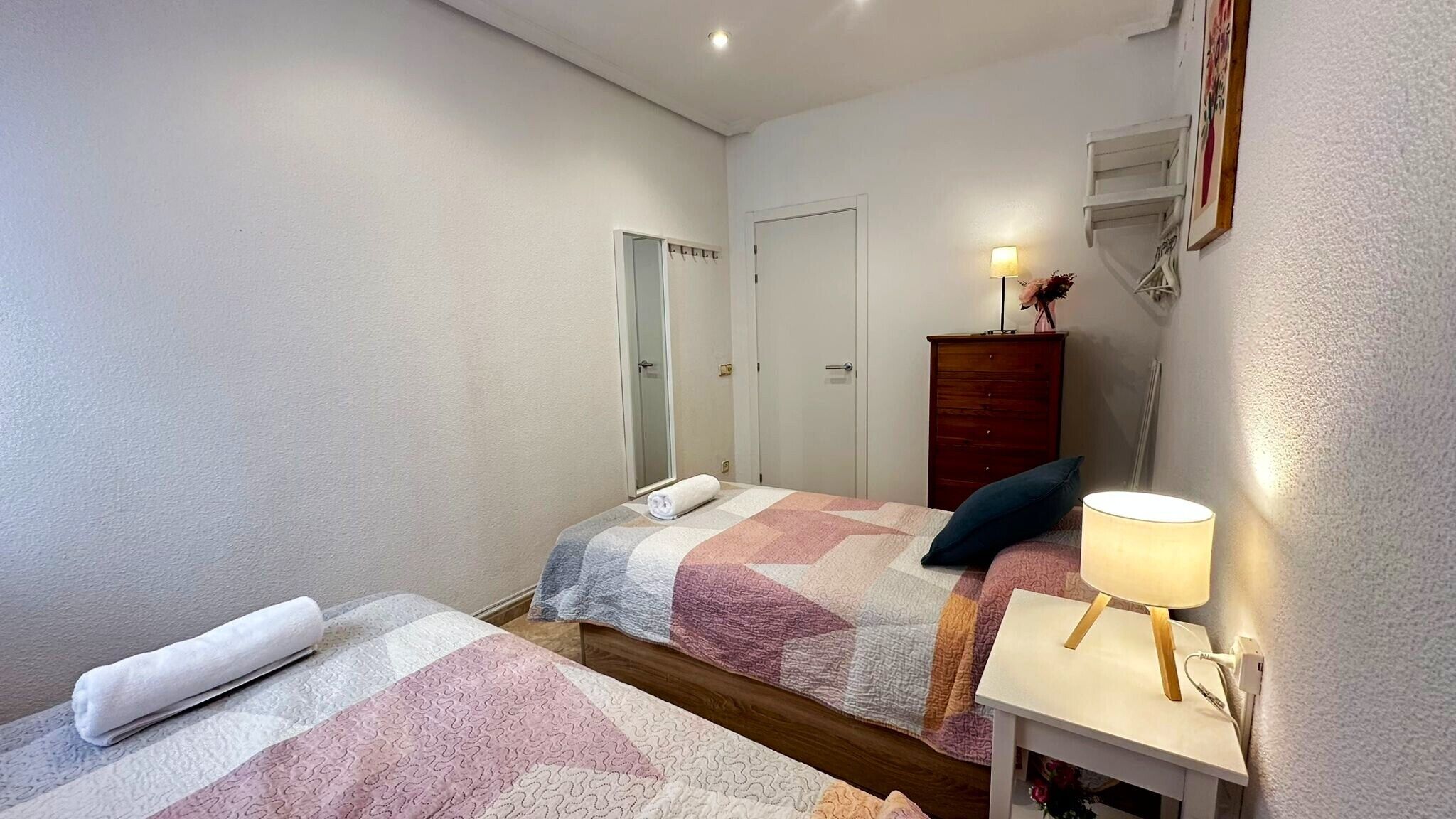 A bedroom with two beds, a dresser, a lamp, and a mirror.