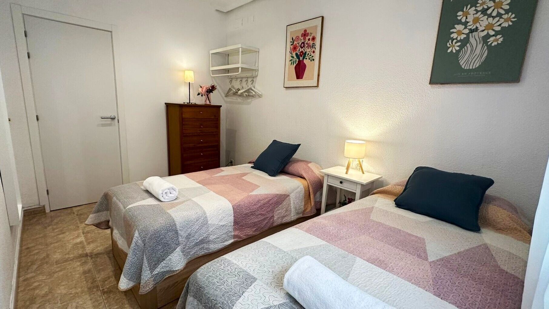 Habitación de hotel con dos camas, un aparador, una mesita de noche, una lámpara, una puerta y un adorno de pared.