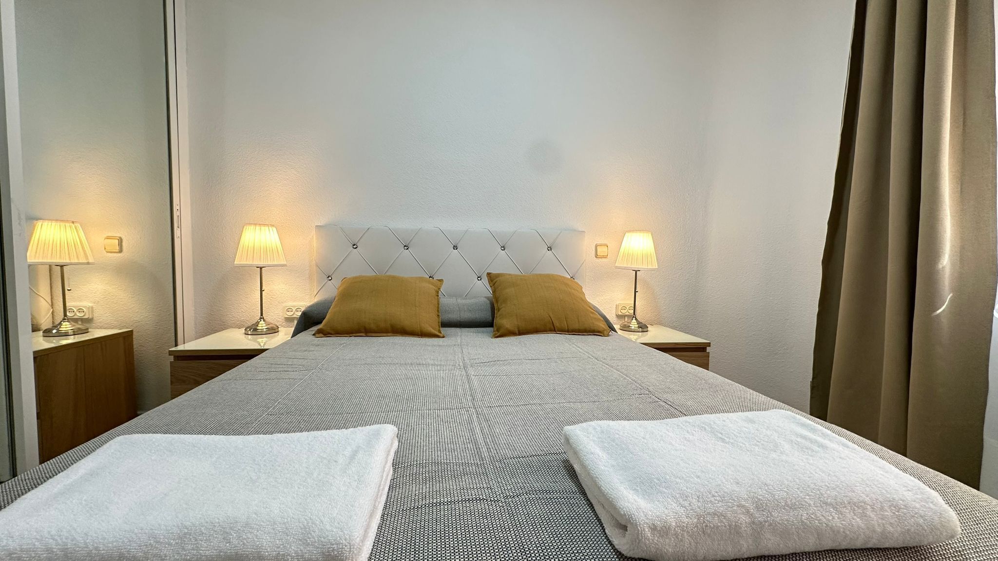 Habitación de hotel con una cama grande, dos mesitas de noche con lámparas y un cabecero con diseño de diamantes.