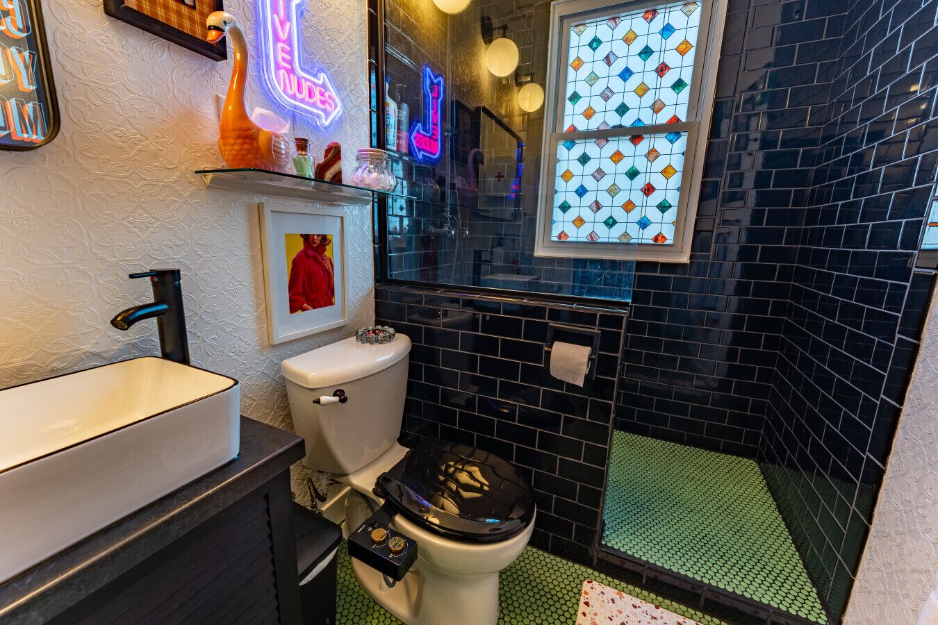 Ein kleines Badezimmer mit einem weißen Waschbecken, einer Toilette und einer Duschkabine mit grün gefliestem Boden.