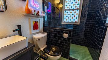 Ein kleines Badezimmer mit einem weißen Waschbecken, einer Toilette und einer Duschkabine mit grün gefliestem Boden.