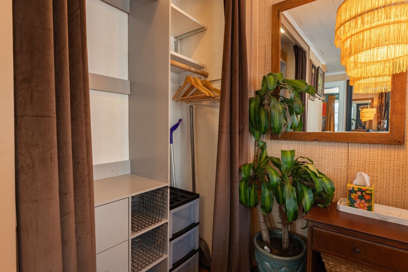 Quarto de hotel com closet amplo, uma planta em vaso, um espelho e uma mesinha de cabeceira com caixa de lenços.