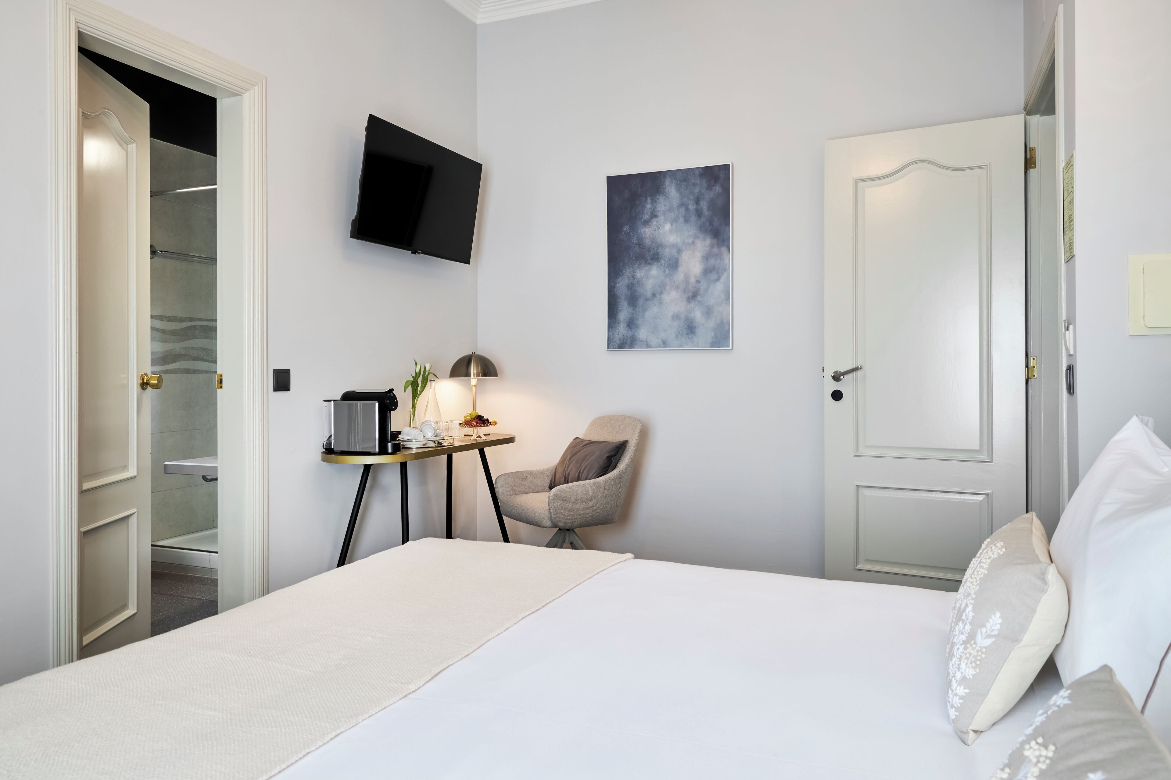 Ein Hotelzimmer mit einem Bett, einem Schreibtisch mit Lampe, einem Sessel, einem Fernseher und einer Tür.