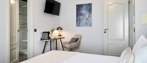 Ein Hotelzimmer mit einem Bett, einem Schreibtisch mit Lampe, einem Sessel, einem Fernseher und einer Tür.