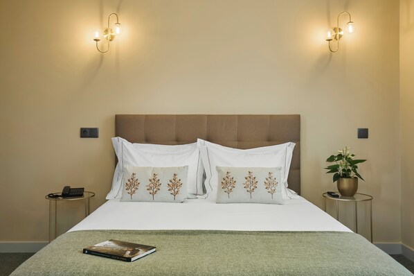 Une chambre d’hôtel avec un grand lit, deux tables de chevet, une lampe fixée au mur et une plante en pot.