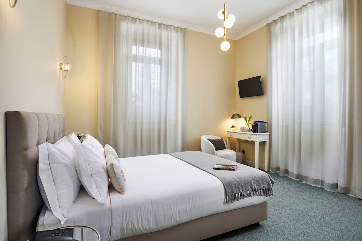 A hotel room with a bed, a desk, a chair, a TV, and a window with curtains.