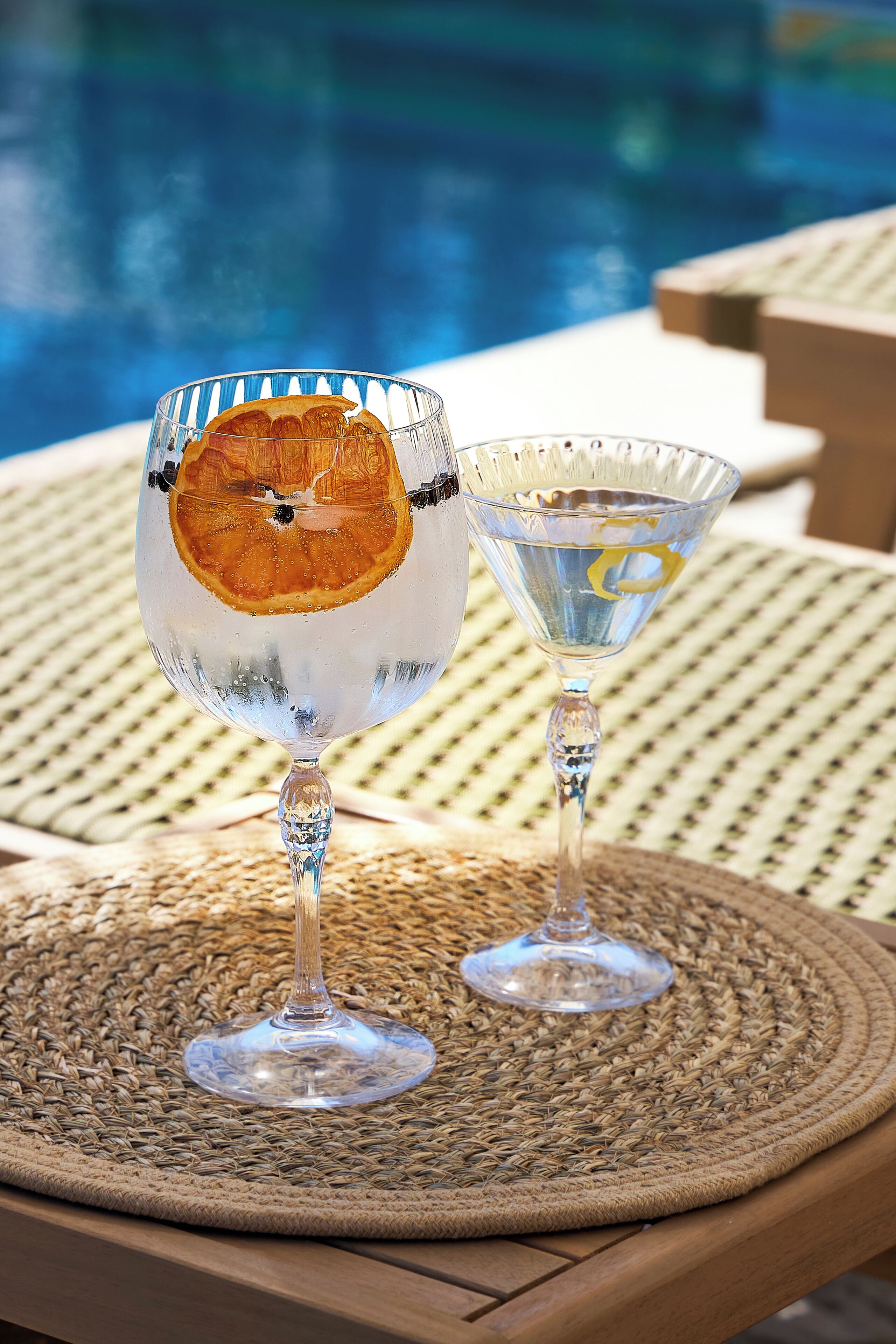 Dos vasos transparentes sobre un tapete tejido junto a una piscina.