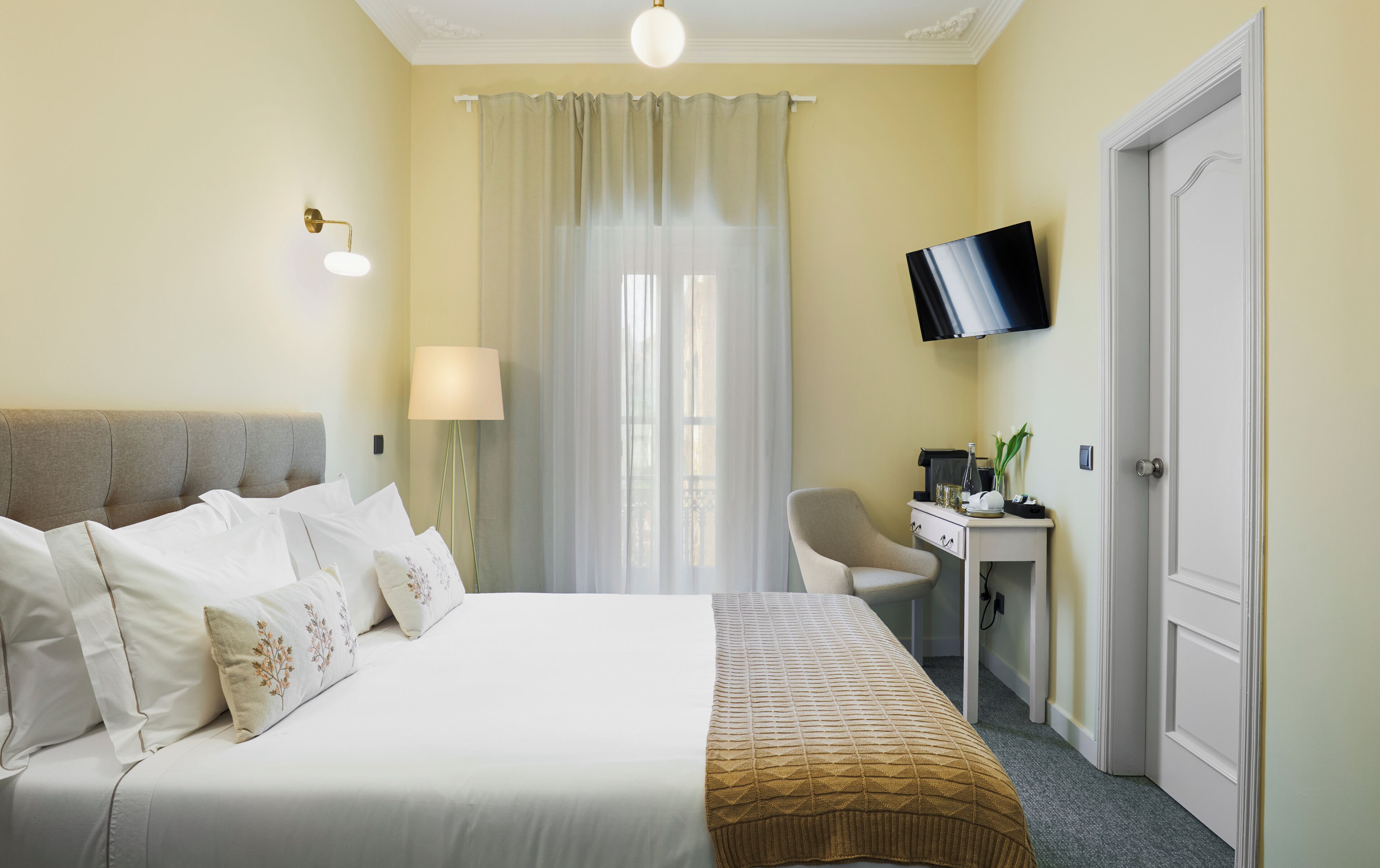Una camera d'albergo con un letto, una scrivania, una sedia, una televisione e una porta.