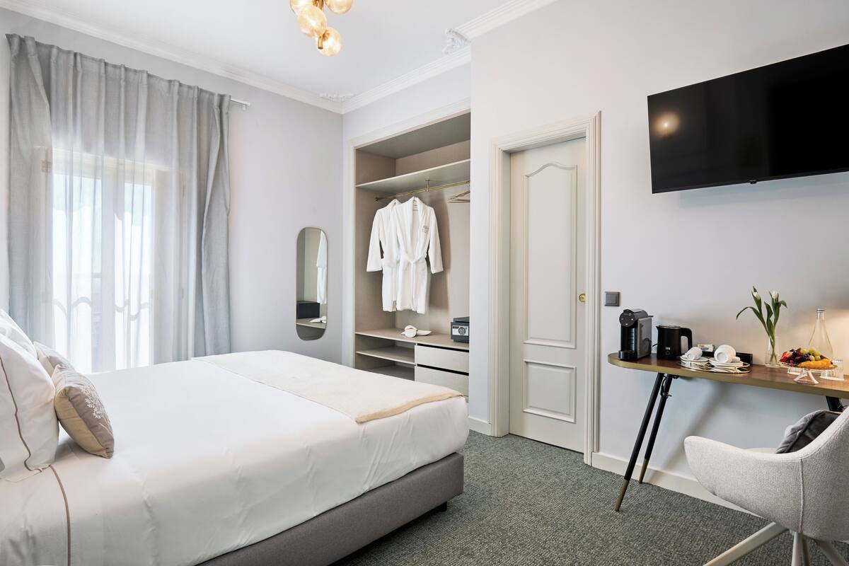A hotel room with a bed, a desk with a coffee maker, a TV, and a closet with hanging robes.