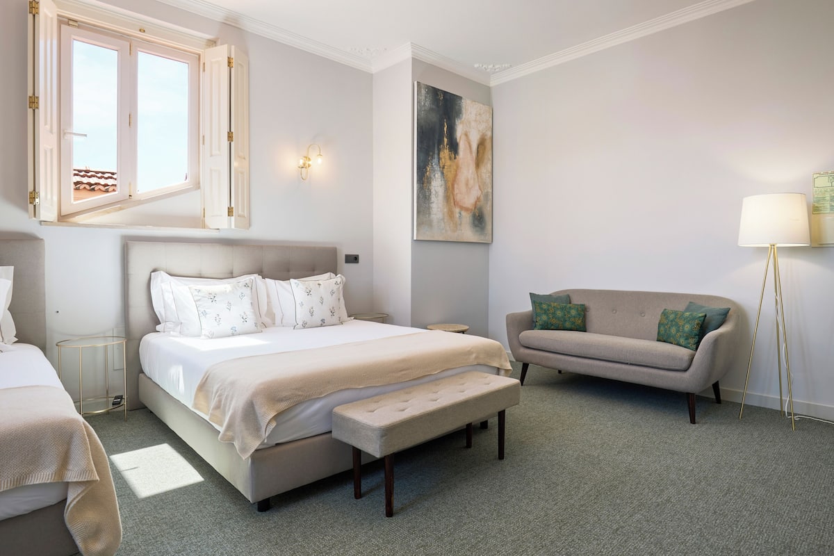 A bedroom with a large bed, a bench, a sofa, and a standing lamp.