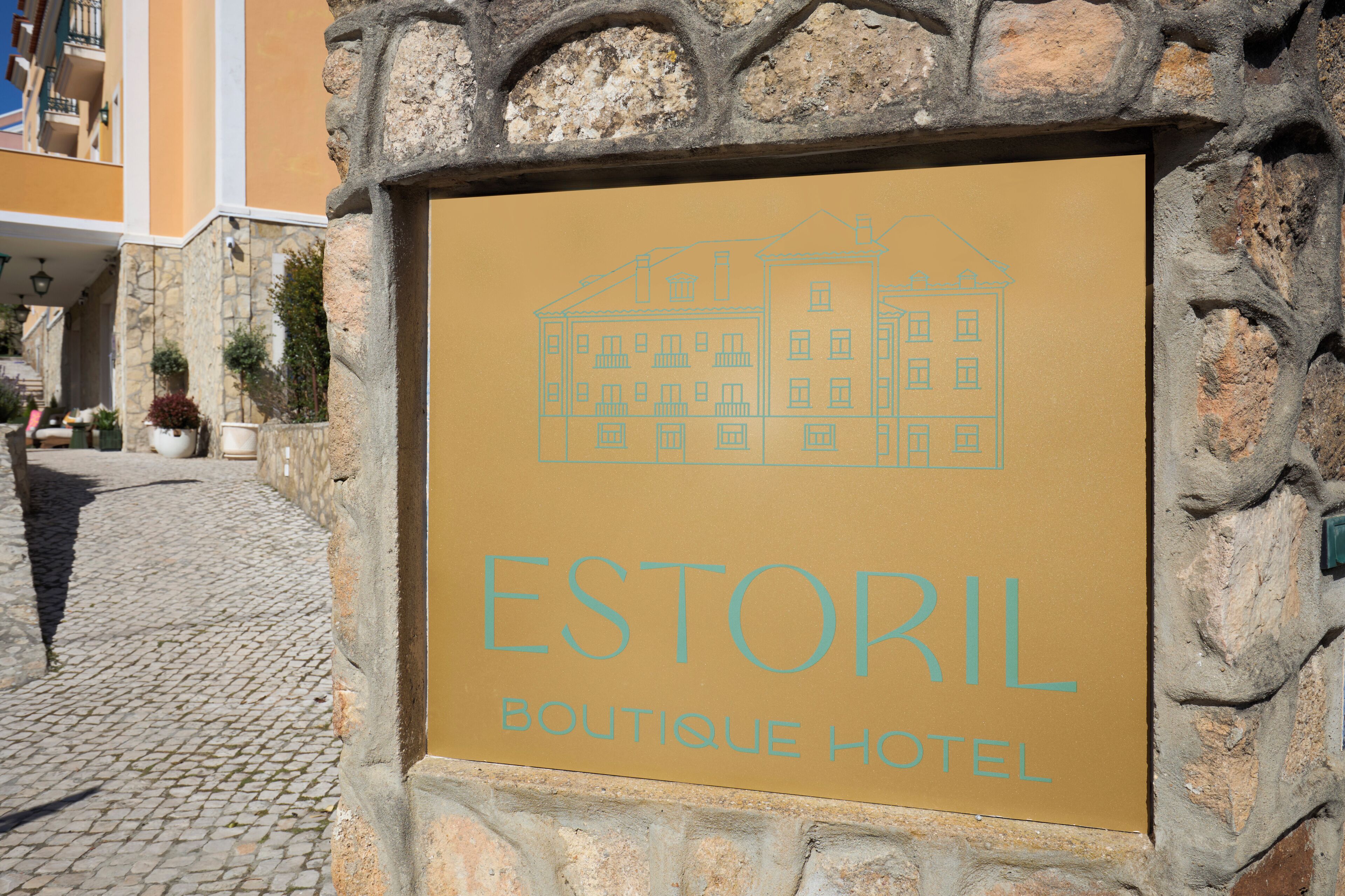 Skilt for Estoril Boutique Hotel med en enkel tegning af en bygning og hotellets navn.