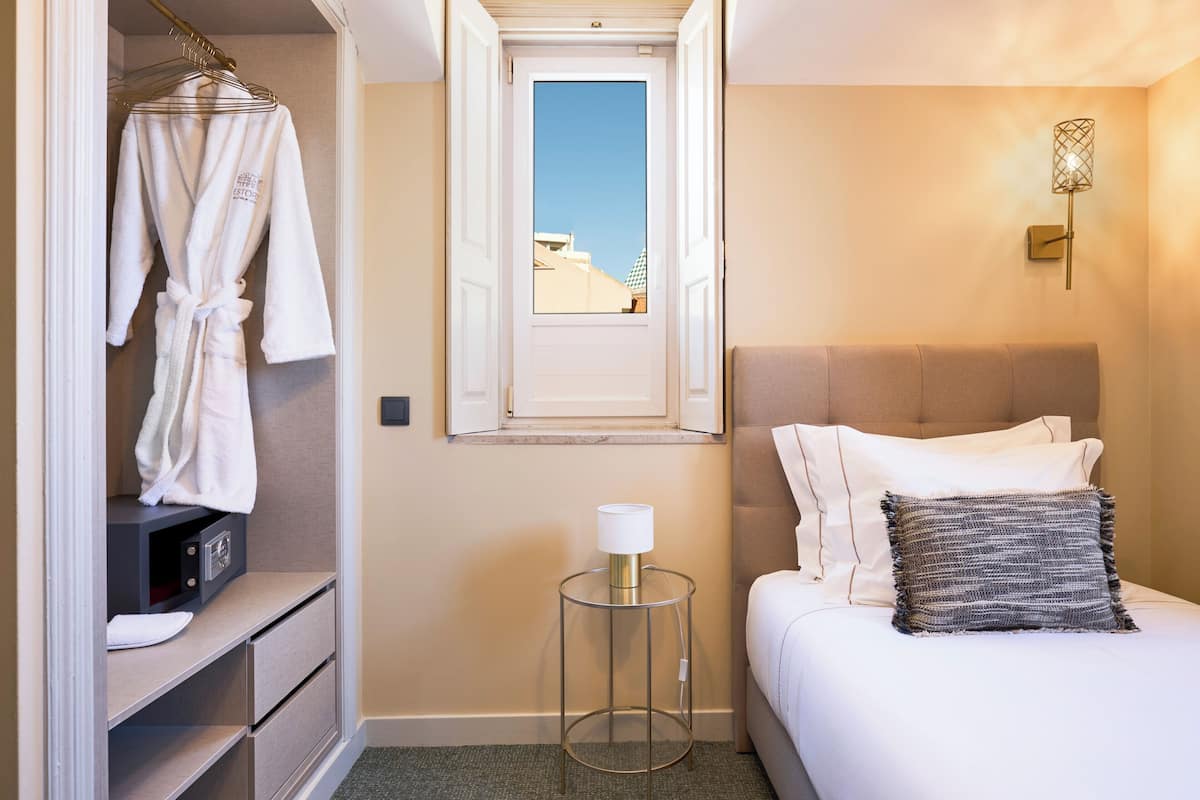 A hotel room with a bed, a bedside table with a lamp, a wardrobe, and a window with a view.