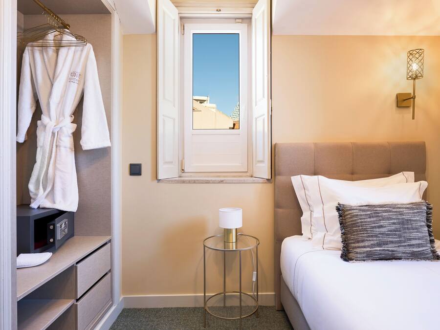 Habitación de hotel con cama, mesita de noche con lámpara, armario y ventana con vistas.
