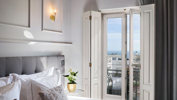A hotel room with a bed, a potted plant, a wall-mounted light fixture, and a view through an open door. - Estoril Boutique Hotel - Adults only (Cascais)