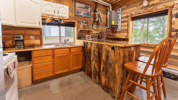 A rustic cabin interior with wooden walls, a kitchen with a sink and cabinets, a coffee maker, and a window overlooking greenery. - Cozy 1BR Lakefront Retreat on Rice Lake – Sleeps 6 | Fishing & Snowmobile Paradise (Spooner)