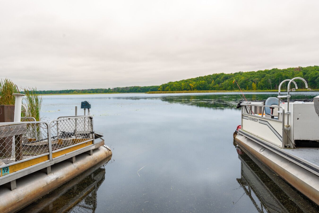 A calm river with a dock, a boat named 'KENNEDY,' and a forested shoreline.