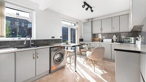 Eine moderne Küche mit integriertem Waschmaschine, einem Essbereich mit Tisch und Stühlen und großen Fenstern, die für natürliches Licht sorgen.