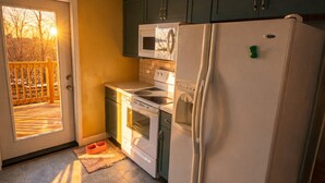 Eine Küche mit Kühlschrank, Backofen, Mikrowelle und einer Tür, die auf eine Terrasse führt.
