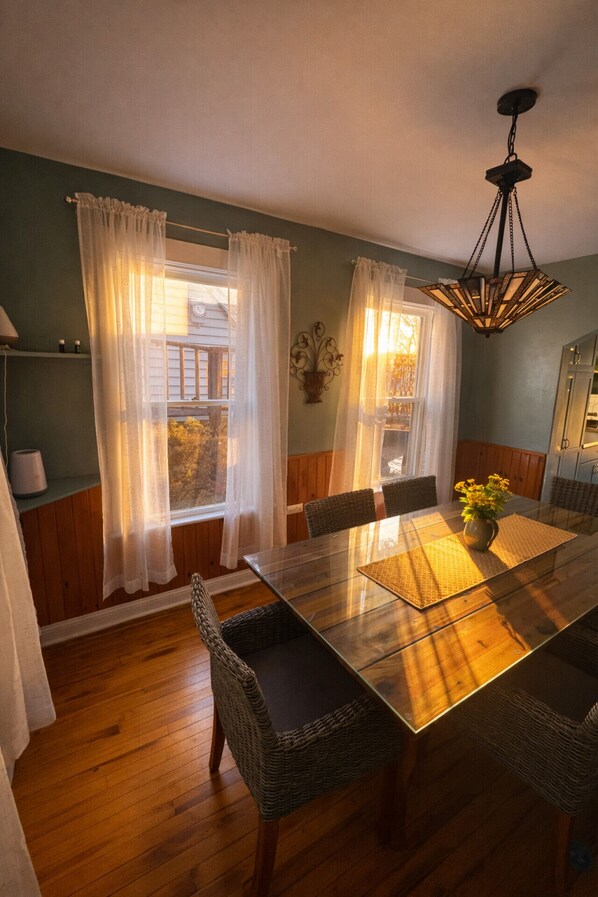 Un comedor con una mesa de vidrio, sillas de mimbre y un colgador de techo.