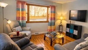 Ein Wohnzimmer mit zwei Sofas, einem Couchtisch, einem Fernseher und einem Fenster mit Vorhängen.