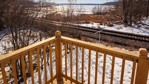 Eine Holzterrasse mit Blick auf eine verschneite Landschaft und ein Bahnweg.